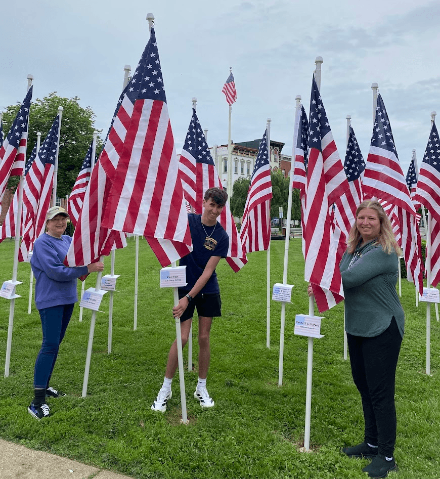 Three volunteers stand among Flags of Honor, each holding a flagpole